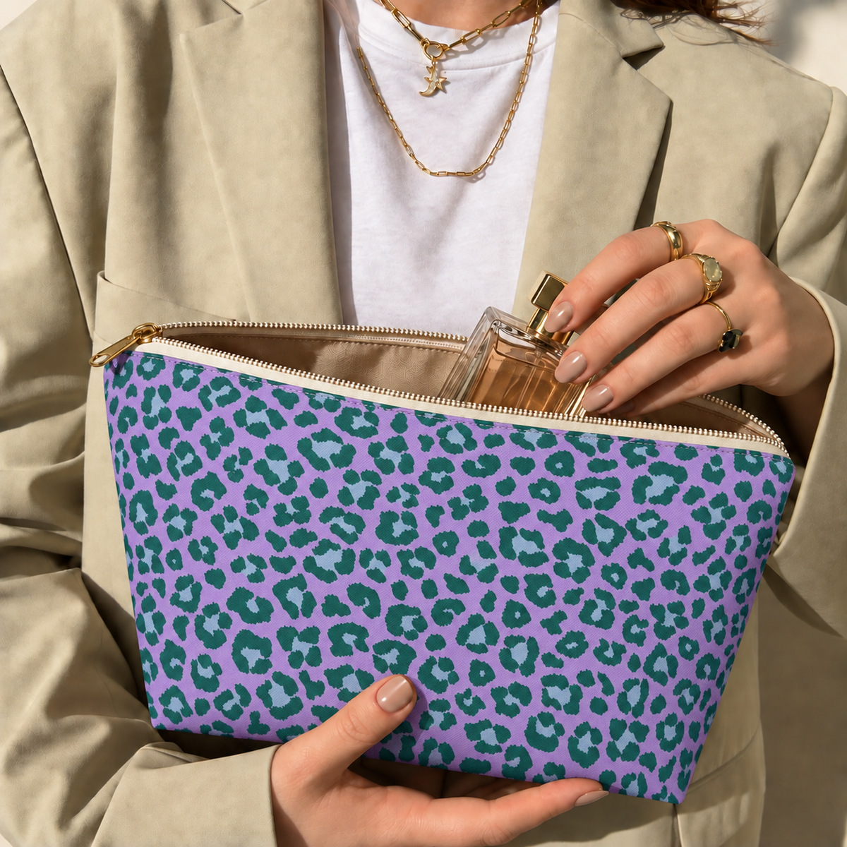 Hands holding the purple green leopard print makeup bag with a perfume bottle inside