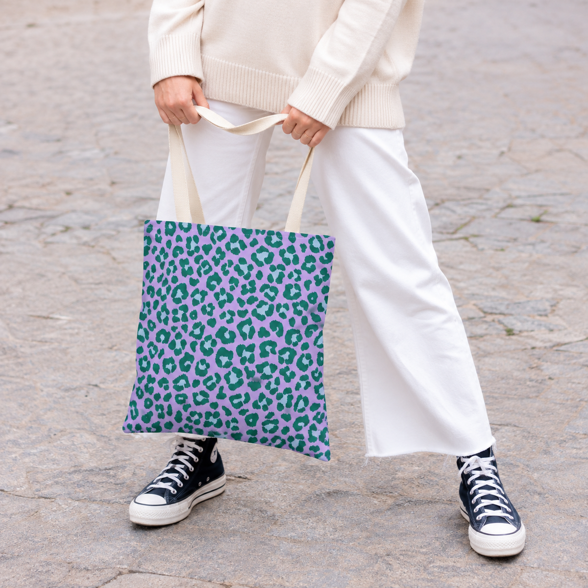 Woman in white trousers carrying the purple green leopard print tote bag