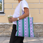 Woman walking with the purple green striped tote bag on her shoulder and an iced drink