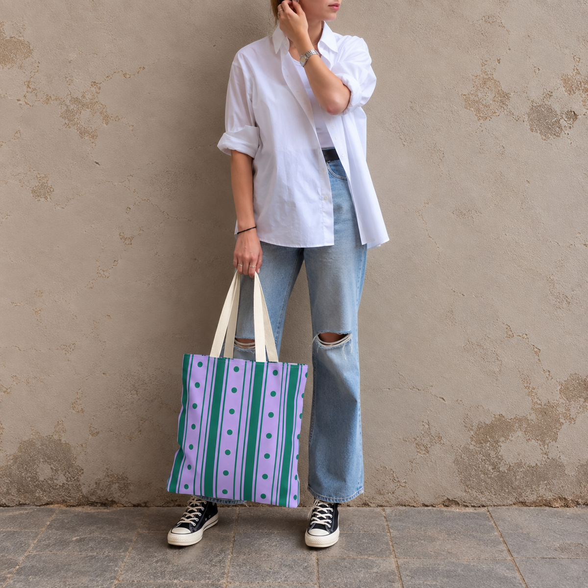 Woman in a white shirt and jeans holding the purple green striped tote bag