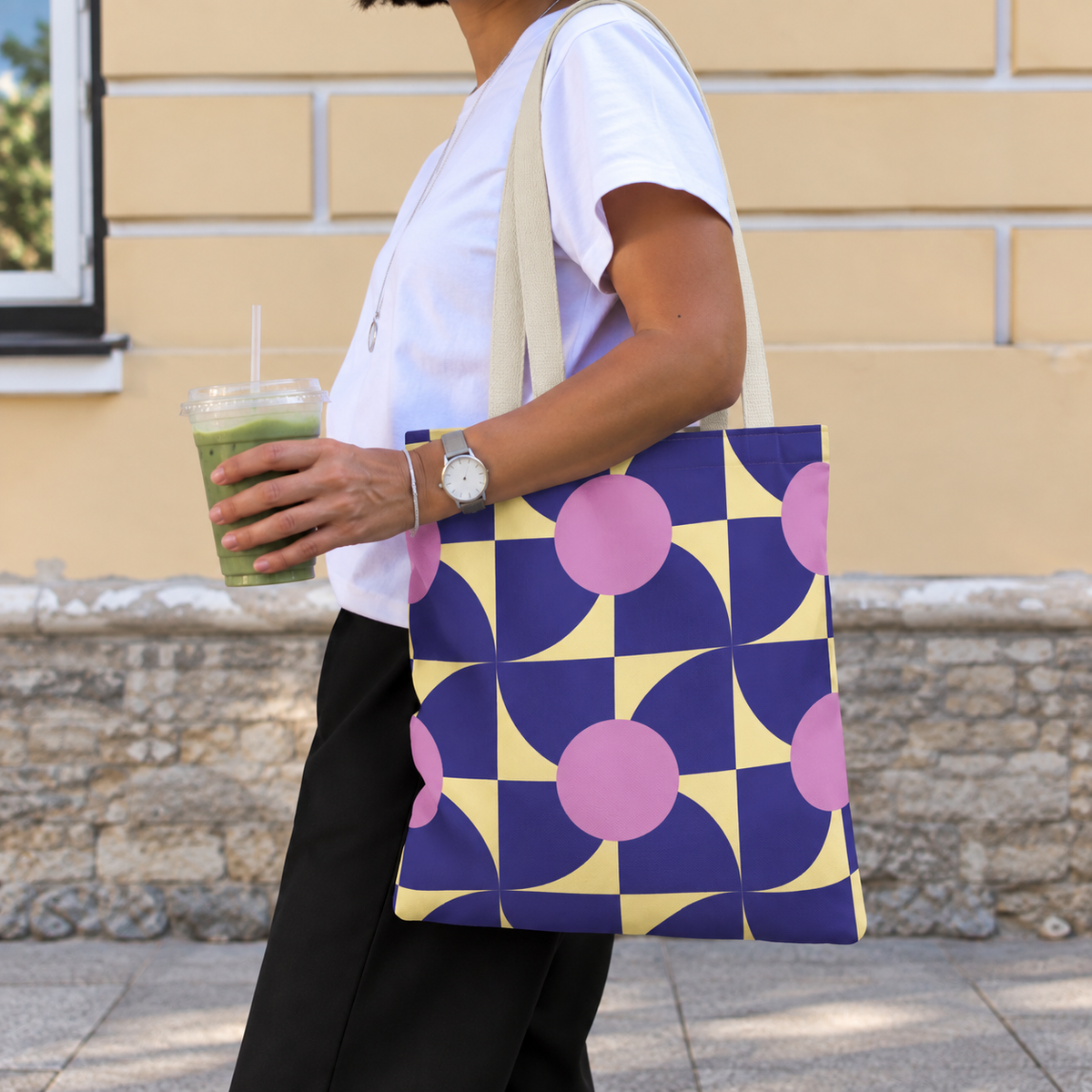 Woman carrying the purple pink geometric tote bag on her shoulder while holding a drink