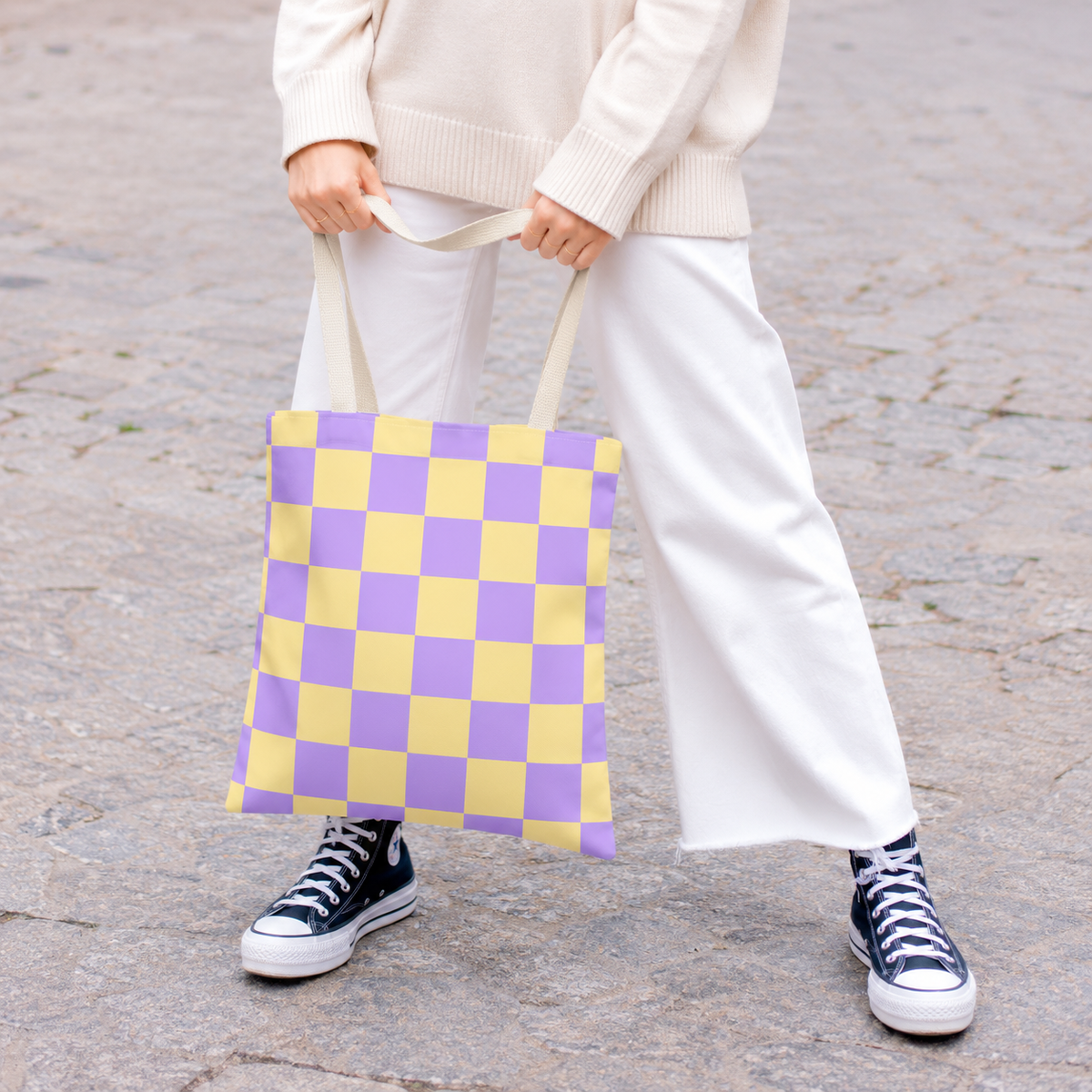 Woman in white trousers holding the purple yellow checkered tote bag by the handles