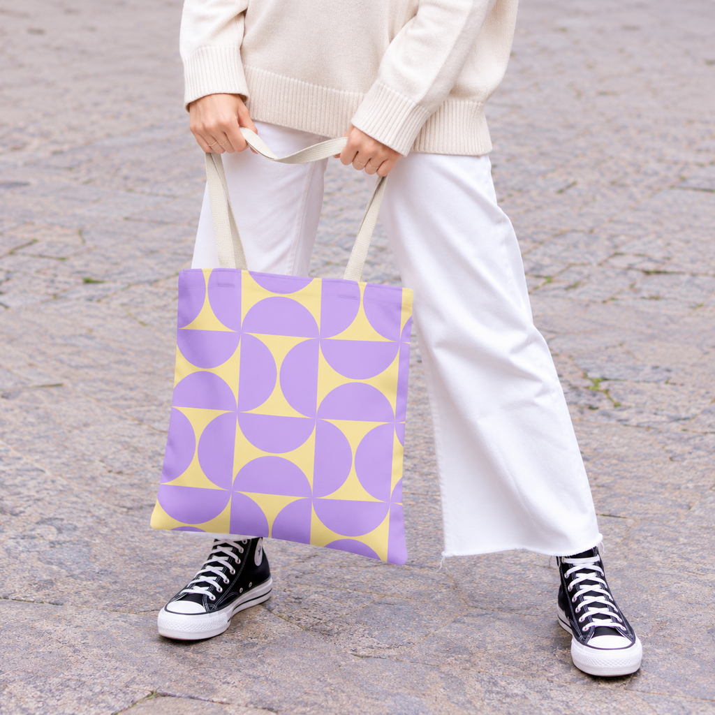 Woman in white trousers holding the purple yellow geometric tote bag by the handles