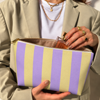 Hands holding the open Purple Yellow Striped makeup bag filled with cosmetics