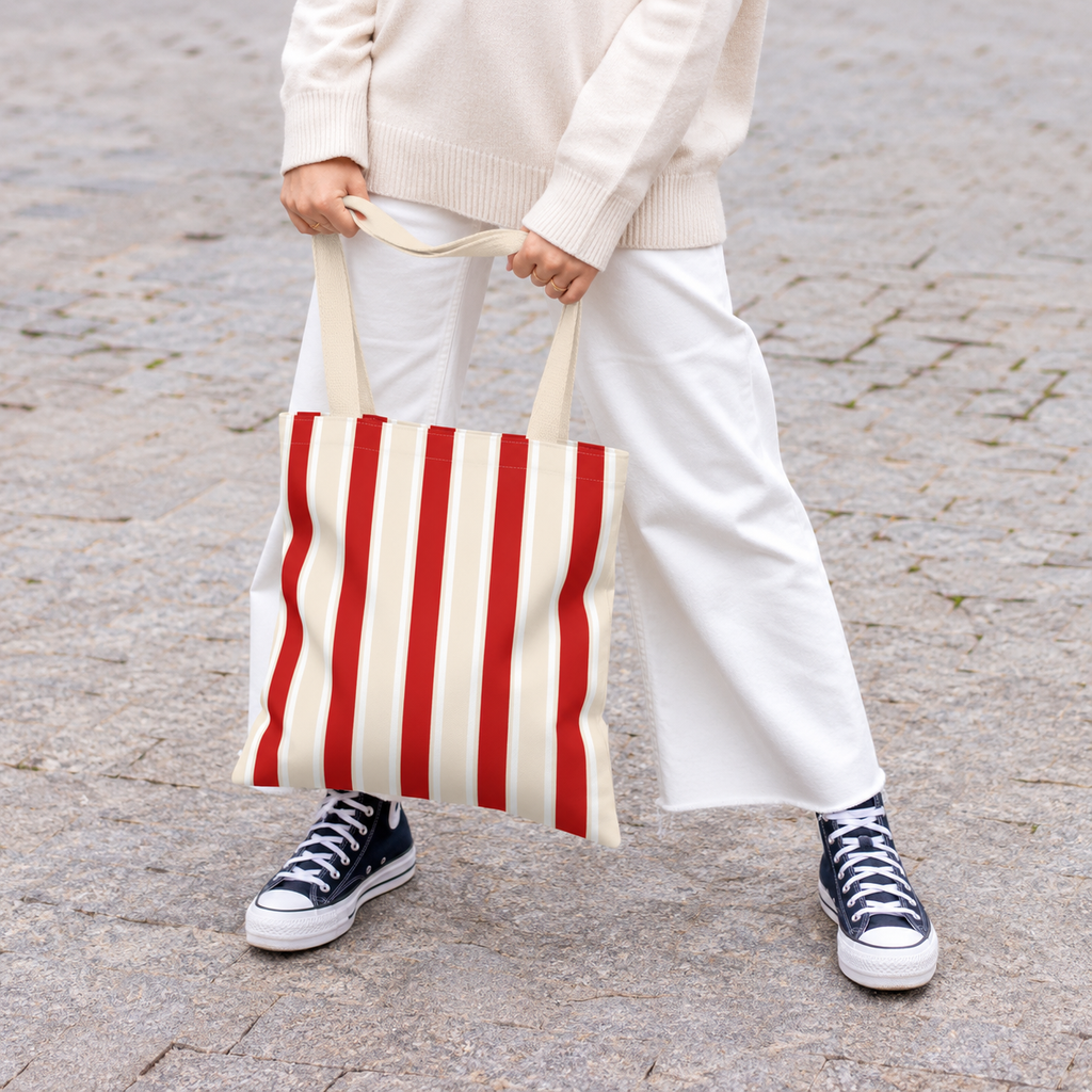 Woman in white trousers holding the red cream striped tote bag by its handles