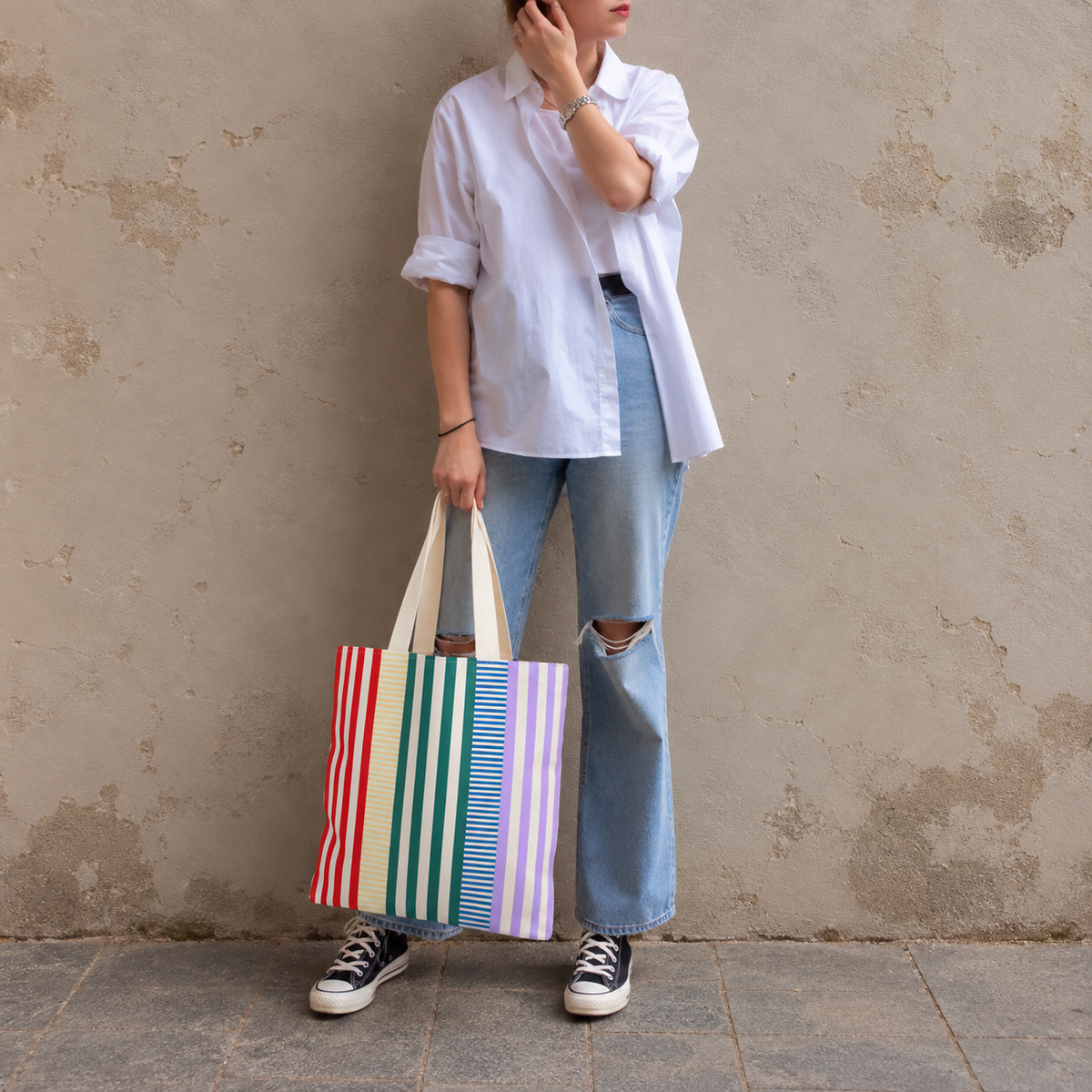 Woman in a white shirt and jeans holding the red green lavender striped tote bag