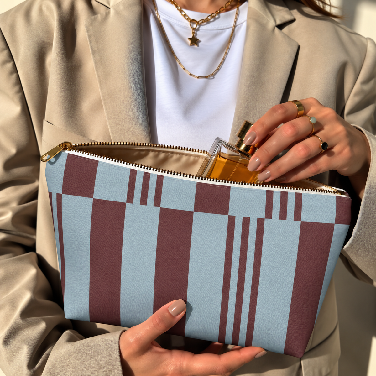 Model in a beige blazer taking a product out of the open sky blue burgundy block striped makeup bag