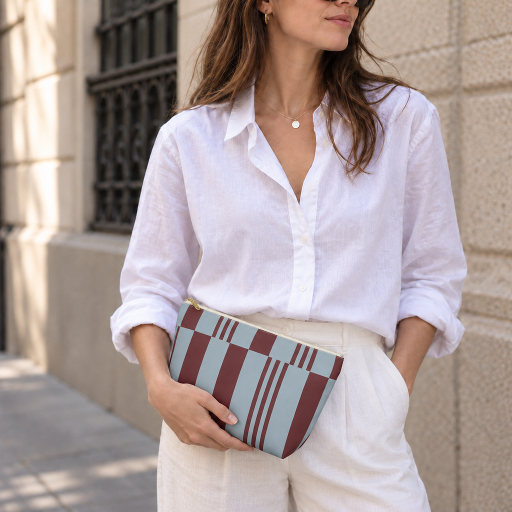 Model in a white shirt holding the sky blue burgundy block striped makeup bag as a clutch