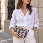 Model in a white shirt holding the sky blue burgundy block striped makeup bag as a clutch