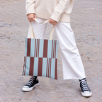 Model holding the sky blue burgundy block striped tote bag in front of white trousers