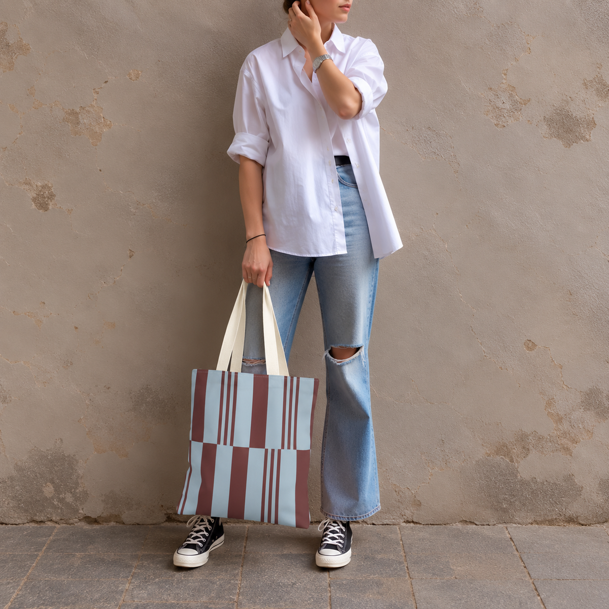 Model in jeans and a white shirt standing with the sky blue burgundy block striped tote bag