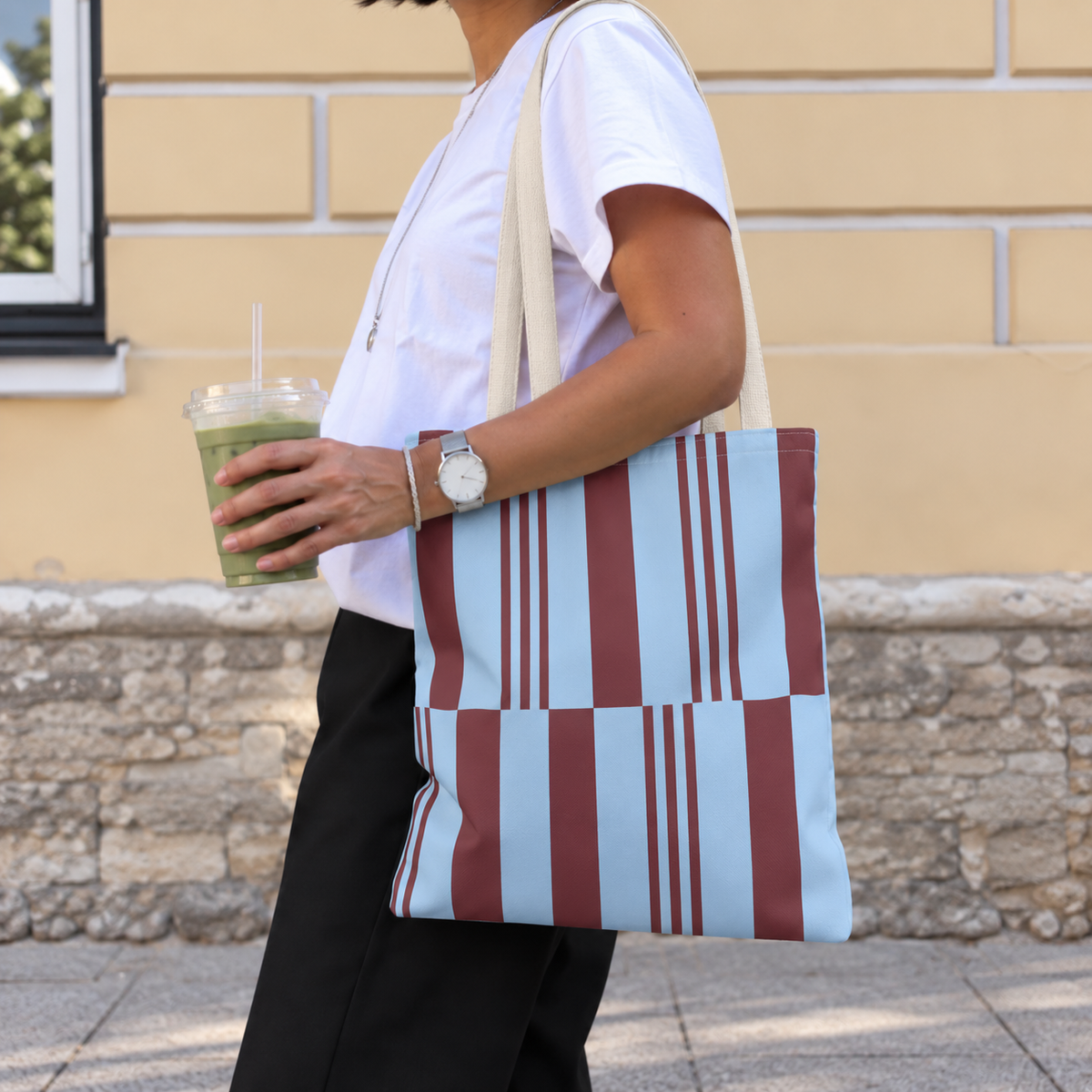 Side view of a model carrying the sky blue burgundy block striped tote bag on the shoulder