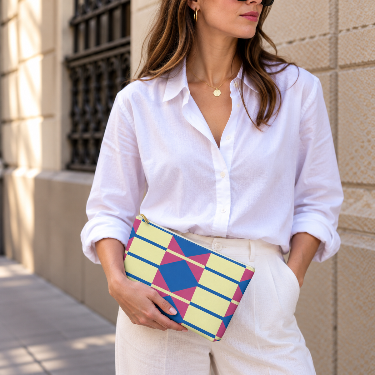 Model in a white shirt holding the yellow pink blue geometric makeup bag at her waist
