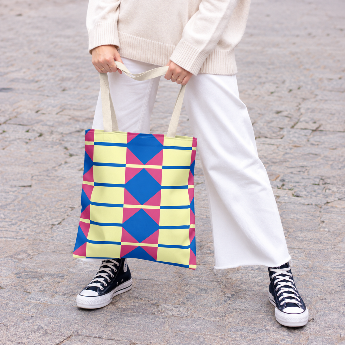 Model in white trousers holding the yellow pink blue geometric tote bag